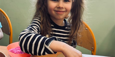 Powiększ grafikę: 4.	Dziewczynka siedzi przy stoliku I wypełnia tekturowe jajko materiałami sypkimi t.j ryż I cieciorka. 