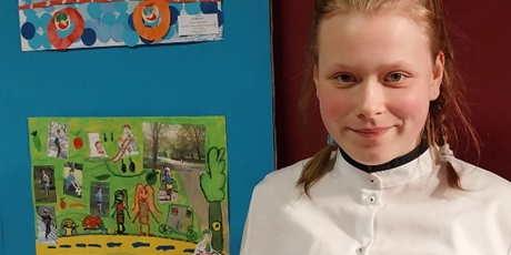 Powiększ grafikę: Dziewczynka stoi na tle swojej nagrodzonej pracy plastycznej.
