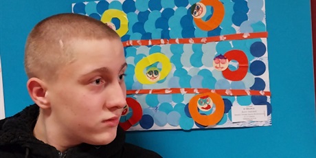Powiększ grafikę: Chłopiec stoi na tle swojej konkursowej pracy plastycznej.