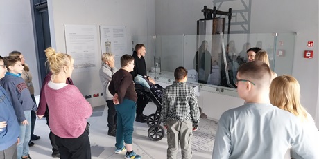 Powiększ grafikę: Stoi grupa uczniów i nauczycieli, przyglądają się rekonstrukcji pompy wodnej.