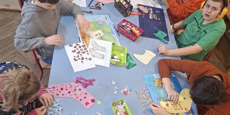 Powiększ grafikę: Zdjęcie zbiorowe zrobione z góry pokazuje uczniów ozdabiających skarpetki za pomocą nalepek, elementów wyciętych przez dziurkacze ozdobne.