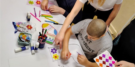 Powiększ grafikę: Zdjęcie zrobione z góry przedstawia uczniów na warsztatach, którzy ozdabiają pokolorowane skarpety elementami ozdobnymi. Dwie panie pomagają chłopcom.