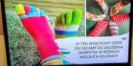 Powiększ grafikę: Tablica multimedialna z prezentacją na której widać stopy z kolorowymi skarpetkami i napis zachęcający do założenia kolorowych skarpetek 21 marca.