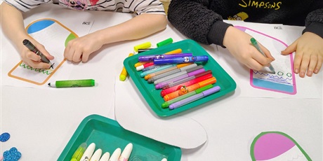 Powiększ grafikę: Zdjęcie pokazuje zbliżenie dziewczynki i chłopca robiącymi mazakami grafomotoryczne wzory na skarpetkach.