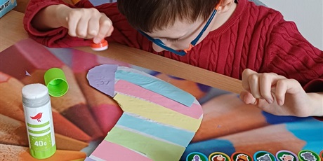 Powiększ grafikę: Zbliżenie na chłopca, który przykleja kolorowe paski na szablon skarpety.