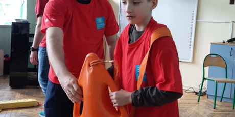 Powiększ grafikę: Uczeń bierze udział w ćwiczeniach z ratownictwa, w ręku trzyma deskę ratowniczą