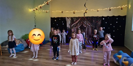 Powiększ grafikę: Dzieci ustawione w  3 szeregach trzymają na paluszkach małe latarki i tańczą.