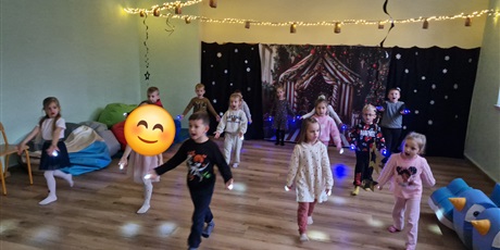 Powiększ grafikę: Dzieci ustawione w  3 szeregach trzymają na paluszkach małe latarki i tańczą.