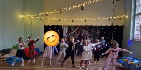 Powiększ grafikę: Dzieci ustawione w  3 szeregach trzymają na paluszkach małe latarki i tańczą. W tle lustro na ścianie.
