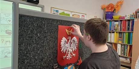 Powiększ grafikę: Uczeń przy tablicy wykonuje zadanie. Przyczepia złotą koronę nad białym orłem na czerwonym tle.
