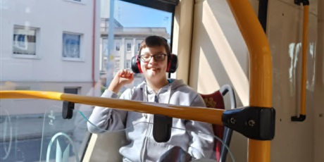 Powiększ grafikę: Chłopiec siedzi w tramwaju i uśmiecha się. W tle zabudowania widoczne przez szybę.