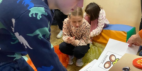 Powiększ grafikę: Na pierwszym planie skrzyneczka skrytka i symbole obrazkowe do wyboru. Chłopiec sięga do skrzyneczki. Kobieta podtrzymuje symbole. W tle sylwetki dzieci.