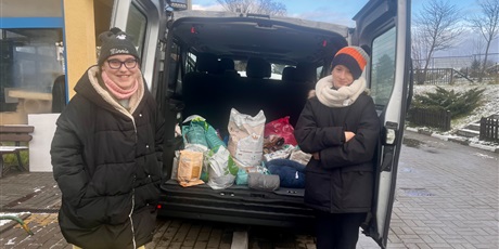 Powiększ grafikę: 5.	Dwoje ludzi stoi przy samochodzie, w tle widać otwarty bagażnik z karmą dla zwierząt