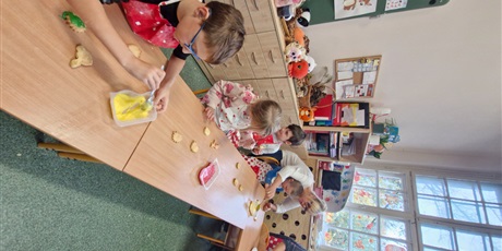 Powiększ grafikę: 7.	Nauczycielka stoi przy stoliku I pokazuje jakie składniki będziemy po kolei dodawać, aby przygotować ciasto.