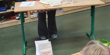 Powiększ grafikę: 7.	Nauczycielka stoi przy stoliku I pokazuje jakie składniki będziemy po kolei dodawać, aby przygotować ciasto.