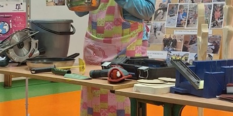 Powiększ grafikę: Uczennica prezentuje naczynia kuchenne. W tle dekoracje.