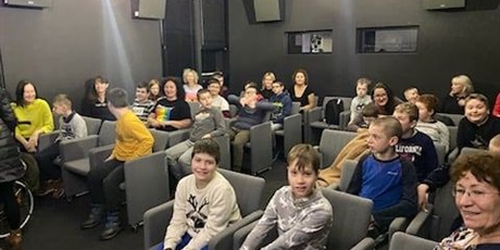 Powiększ grafikę: Uczniowie siedzą w sali kinowej, w tle projektory, zbliżenie na uczniów